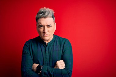 Kırmızı izole edilmiş arka plan üzerinde zarif yeşil tişört giyen yakışıklı, kuşkucu ve gergin genç bir adam. Yüzünde çapraz kollarla onaylanmayan bir ifade var. Negatif kişi.