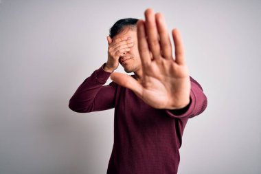 Genç, yakışıklı, İspanyol gömlekli bir adam beyaz, izole edilmiş arka planda dikiliyor, gözleri ellerle kaplıyor ve üzgün ve korku ifadeleriyle jest yapıyor. Utanç verici ve olumsuz bir kavram..