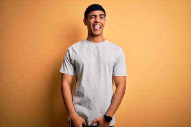 Yakışıklı Afro-Amerikan sporcusu spor giyer sarı arka plan üzerine spor giyer, kameraya seksi bir ifadeyle bakar, neşeli ve mutlu bir yüzle..