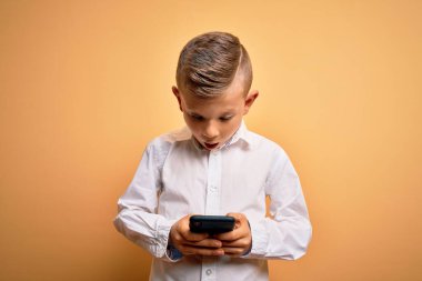 Küçük beyaz bir çocuk akıllı telefon kullanıyor ve ekranda telefon ekranına bakıyor. Şaşırmış bir yüzle korkmuş ve korku ifadesinden korkuyor.