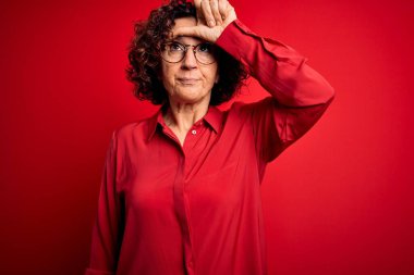 Orta yaşlı güzel kıvırcık saçlı kadın kırmızı arka planda günlük gömlek ve gözlük takıyor. Alnında parmakları olan insanlarla dalga geçiyor. Ezik hareketler yapıyor, alay ediyor ve hakaret ediyor..