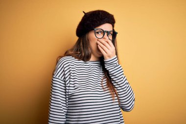 Genç, güzel esmer kadın Fransız beresi takıyor ve sarı arka planda gözlük takıyor. Kokuşmuş ve iğrenç bir koku alıyor. Dayanılmaz bir koku. Kötü kokuyor.