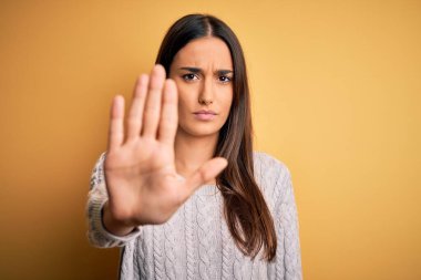 Sarı arka planda beyaz süveter giyen güzel esmer kadın avucunun içi gibi şarkı söylemeyi kesiyor. Yüzünde olumsuz ve ciddi bir jest olan uyarı ifadesi.