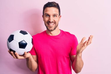 Genç yakışıklı oyuncu futbol topunu soyutlanmış pembe arka planda tutarak başarıyı mutlu bir gülümsemeyle ve kazanan yüz ifadesiyle kutluyor.