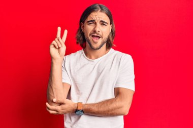 Sıradan kıyafetler giyen, gülen, kameraya göz kırpan, zafer işareti yapan genç yakışıklı bir adam. İki numara.. 