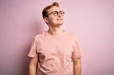 Genç, yakışıklı, günlük tişört giyen, izole edilmiş pembe arka planda duran, gülümseyen ve başka tarafa bakıp düşünen kızıl saçlı adam..