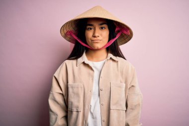 Geleneksel Asya şapkası takan genç ve güzel bir kadın izole edilmiş pembe arka plan ve yüzünde ciddi bir ifade var. Basit ve doğal bir şekilde kameraya bakıyorsun..