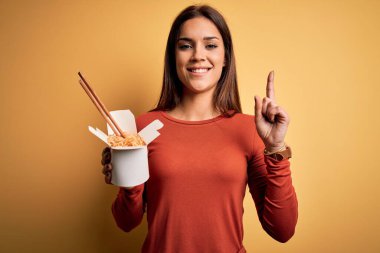 Genç, güzel esmer kadın yemek çubuklarıyla erişte yiyor. Bir fikir ya da soru işareti ile şaşırmış, mutlu yüzle bir numara.