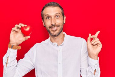 Kalbini tutan yakışıklı genç adam gülümsüyor mutlu bir şekilde elini ve parmağını yana doğru gösteriyor. 