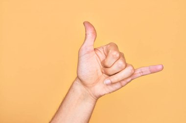 Kafkas genci parmaklarını izole edilmiş sarı arka planda gösteriyor Hawaii Shaka selamlama hareketi, telefon ve iletişim sembolü.