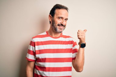 Orta yaşlı, beyaz çizgili tişört giyen, izole edilmiş beyaz arka planda duran mutlu yüzlü ve baş parmağıyla yüzünü gösteren, orta yaşlı, beyaz bir adam..