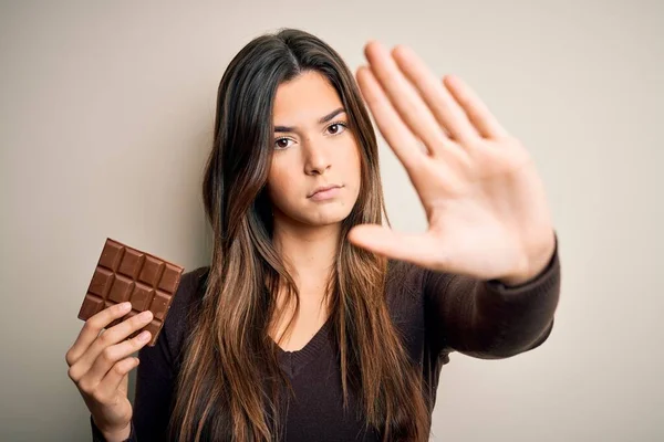 若いです美しいです女の子保持甘いですバーのチョコレート上に隔離された白い背景で手を開きます停止記号で真剣で自信を持って式 防衛ジェスチャー — ストック写真