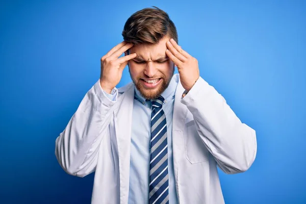 Young blond therapist man with beard and blue eyes wearing coat and tie over background with hand on head for pain in head because stress. Suffering migraine.