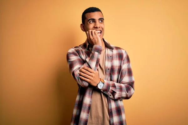 年轻英俊的非洲裔美国男人穿着休闲衫站在黄色的背景上 看起来很紧张 双手放在咬指甲的嘴上 焦虑问题 — 图库照片