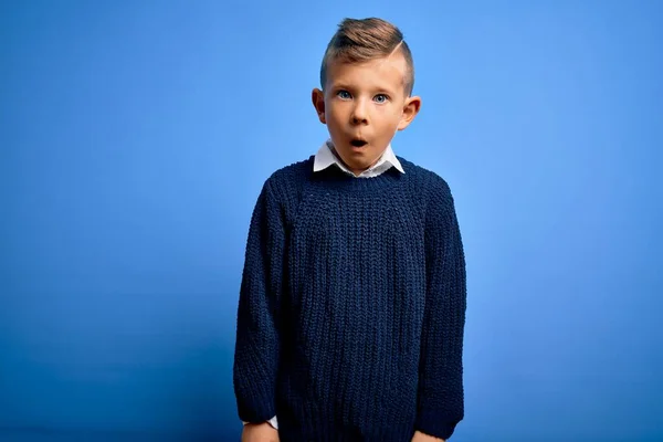 若いですCaucasian子供とともに青い目身に着けている冬のセーター上青い背景恐怖とショックで驚きの表情 恐怖と興奮した顔 — ストック写真
