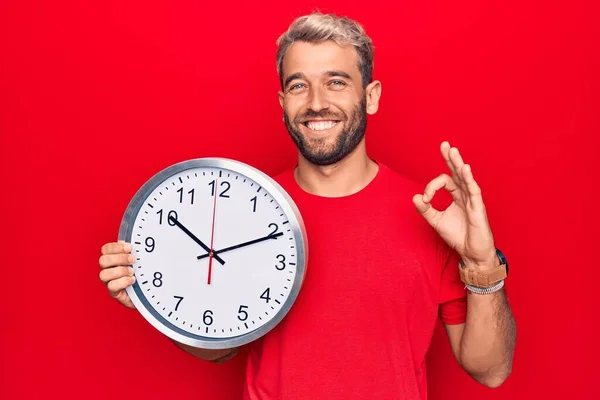 Sakallı Yakışıklı Sarışın Adam Kırmızı Arka Planda Büyük Bir Saat — Stok fotoğraf