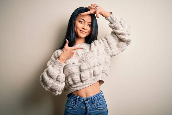 若い美しい中国の女性は幸せな顔を持つ手と指でフレームを作る孤立した白い背景笑顔の上にカジュアルなセーターを着ています 創造性と写真の概念 — ストック写真