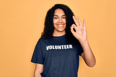Genç Afro-Amerikalı kıvırcık kadın gönüllü olarak gönüllü tişört giyiyor. Parmaklarıyla imza atıyor. Mükemmel bir sembol.