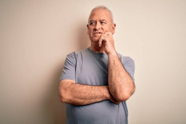 Orta yaşlı, beyaz tişörtlü yakışıklı bir adam izole edilmiş beyaz arka plan üzerinde duruyor, elleri çenesinde soru sormayı düşünüyor, düşünceli bir ifade. Düşünceli bir yüzle gülümsüyor. Şüphe kavramı.