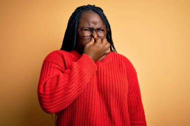Sarı arka planda sıradan süveter giyen Afro-Amerikan kadın pis ve iğrenç bir koku alıyor, nefesini burnunda tutuyor. Kötü kokuyor.