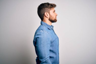 Sakallı, mavi gözlü, sıradan bir kot gömlek giyen, rahat bir görünüm takınan, kendine güvenen ve gülümseyen genç, yakışıklı sarışın bir adam..