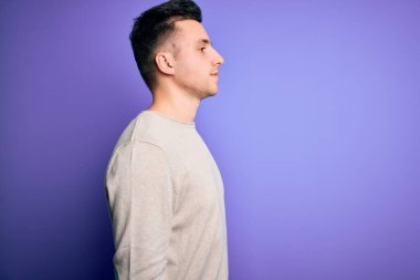 Mor izole arka plan üzerine günlük süveter giyen yakışıklı beyaz adam yan yana bakıyor, rahat profil pozu veriyor, kendine güvenen bir gülümsemesi var..