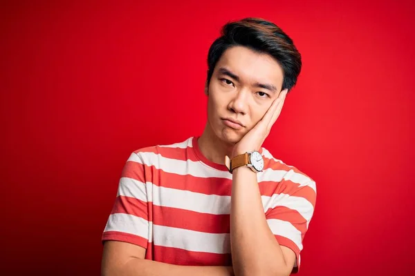 若いですハンサムな中国人男性身に着けていますカジュアルストライプTシャツ上に立って赤い背景思考疲れていると退屈でうつ病問題とともに交差腕 — ストック写真