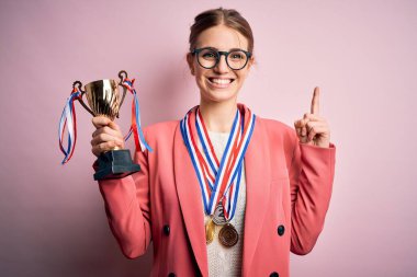 Pembe arka planda madalyalar takan genç, güzel, kızıl saçlı bir kadın bir fikir ya da soru işareti ile şaşırdı.