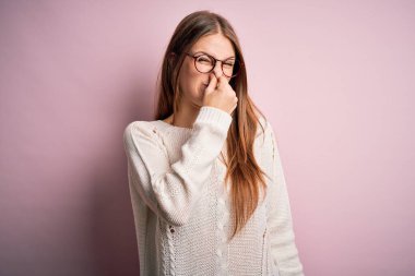 Genç, güzel, kızıl saçlı bir kadın pembe arka planda günlük süveter ve gözlük takıyor. Kokuşmuş ve iğrenç bir koku alıyor. Dayanılmaz bir koku. Kötü kokuyor.