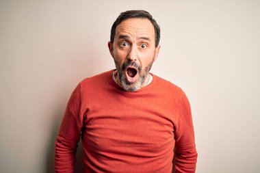 Orta yaşlı, turuncu bir süveter giyen, beyaz arka plan üzerinde duran, korkmuş, şaşırmış, şaşırmış, ifade, korku ve heyecanlı yüz ifadesiyle şoka uğramış orta yaşlı bir adam..
