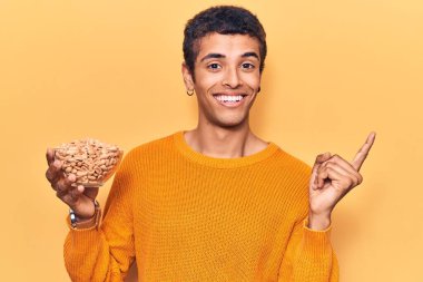 Fıstık tutan genç Afrikalı Amerikalı adam gülümsüyor mutlu bir şekilde elini ve parmağını yana doğru gösteriyor. 