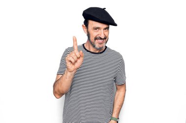 Orta yaşlı yakışıklı bir adam çizgili tişört ve beyaz arka planda Fransız beresi takıyor. Bir fikir veya soruyla gülümsüyor ve mutlu bir yüzle işaret ediyor.