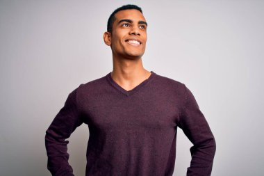 Beyaz arka plan üzerine gündelik süveter giyen yakışıklı Afro-Amerikalı genç adam yüzünde gülümseme, doğal bir ifade ile yan yana bakıyor. Kendinden emin gülen.