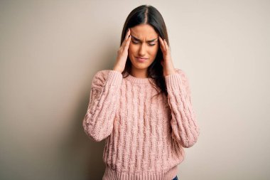 Genç, güzel esmer kadın, izole edilmiş beyaz arka plan üzerine günlük süveter giyiyor. Ağrı ve migren yüzünden baş ağrısı ve stres altında. Ellerini başının üstüne koy..