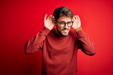 Sakallı, gözlüklü ve süveterli genç bir adam kırmızı arka planda dikilmiş iki elini de kulak hareketi yaparken duymaya çalışıyor, dedikoduya meraklı. İşitme problemi, sağır