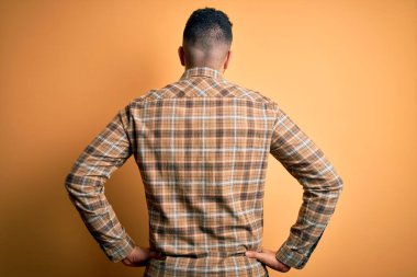 Sarı arka planda dikilip kolları vücudunda olan genç ve yakışıklı bir adam.