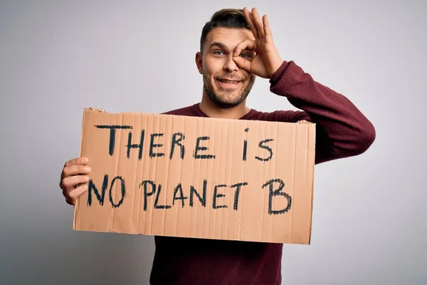 Young activist man holding protest banner for climate change and environment change with happy face smiling doing ok sign with hand on eye looking through fingers