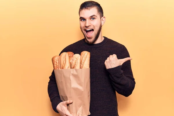 Young Handsome Man Holding Paper Bag Bread Pointing Thumb Side — Stock Photo, Image