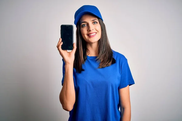 Young delivery woman with blue eyes wearing cap holding smartphone with a happy face standing and smiling with a confident smile showing teeth