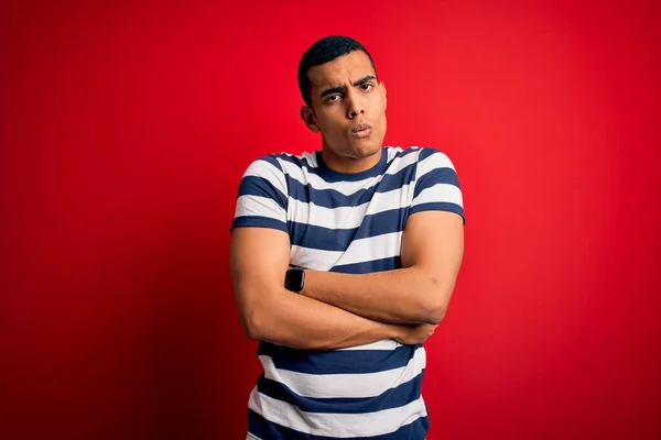 Handsome african american man wearing casual striped t-shirt standing over red background shaking and freezing for winter cold with sad and shock expression on face