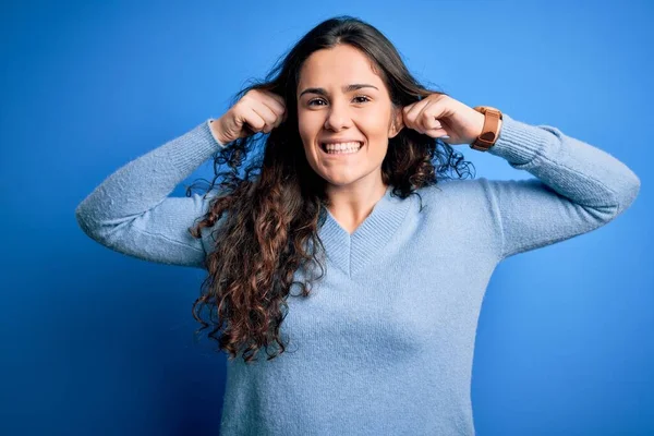 孤立した背景に青いカジュアルなセーターを着て巻き毛の若い美しい女性指で耳を引く笑顔 面白いジェスチャー オーディション問題 — ストック写真