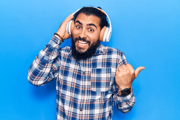 Young Arab Man Listening Music Using Headphones Pointing Thumb Side — Stock Photo, Image