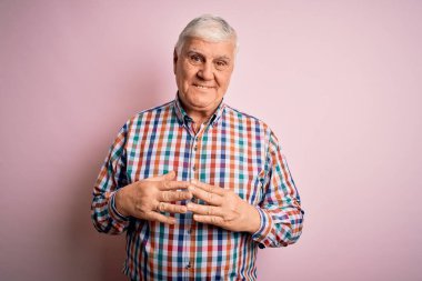 Üst düzey yakışıklı beyaz adam, pembe arka planda rahat ve neşeli bir şekilde gülümseyen pembe elleri ve parmakları birleştirerek, sıradan bir gömlek giyiyor. Başarı ve iyimser