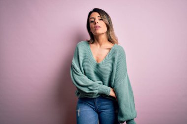 Moda kıyafetleri giyen genç ve güzel bir kadın. Manken, sokak tarzı giyiniyor. Pembe arka planda dikiliyor.