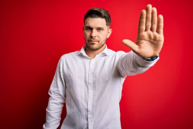 Mavi gözlü, zarif gömlekli, kırmızı izole edilmiş arka planda duran genç iş adamı avucunun içinde şarkı söylemeyi kesiyor. Yüzünde olumsuz ve ciddi bir jest olan uyarı ifadesi.