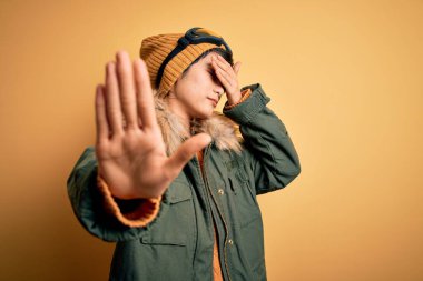 Güzel Asyalı kayakçı kız kar gözlüğü takıyor sarı arka planda kayak gözlüğü takıyor gözleri ellerle örtüyor ve üzgün ve korku ifadeleriyle jest yapıyor. Utanç verici ve olumsuz bir kavram..