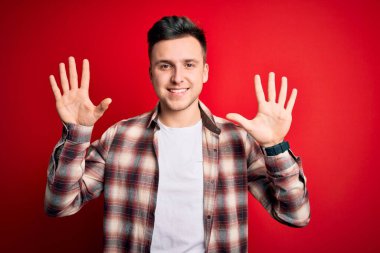 Kırmızı izole edilmiş arka plan üzerine gündelik modern gömlek giyen genç beyaz adam on numarayı gösterirken kendinden emin ve mutlu bir şekilde gülümsüyor..