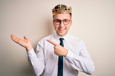 İzole edilmiş arka planda altın taç takan yakışıklı beyaz iş adamı kameraya hayret ediyor ve gülümsüyor..