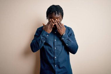 Genç, yakışıklı, Afro-Amerikan bir adam, günlük gömleğini giymiş, beyaz arka plan üzerinde duruyor, yorgunluk ve baş ağrısı için gözlerini ovuyor, uykulu ve yorgun bir ifade takınıyor. Görüş sorunu