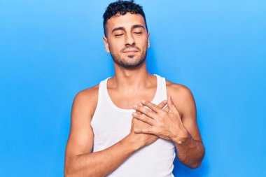 Gündelik kıyafetler giyen genç İspanyol adam elleri göğsünde gülümsüyor, gözleri kapalı ve yüzünde minnet ifadesi var. sağlık kavramı. 